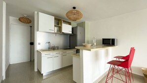 A modern kitchen with white cabinets, a stainless steel sink, a microwave, and a red chair. - Appart Standing vue mer & Marina (Pointe-à-Pitre)