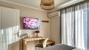 A bedroom with a bed, a desk, a chair, a television, and a window with curtains. - Deluxe Seaside Condo for 6 (Kantia)