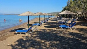 A beach with sun loungers and thatched umbrellas, a clear sky, and a calm sea. - Deluxe Seaside Condo for 6 (Kantia)