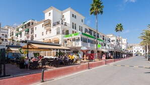 Una calle con terrazas al aire libre en varios cafés y restaurantes, un autobús rojo y palmeras.