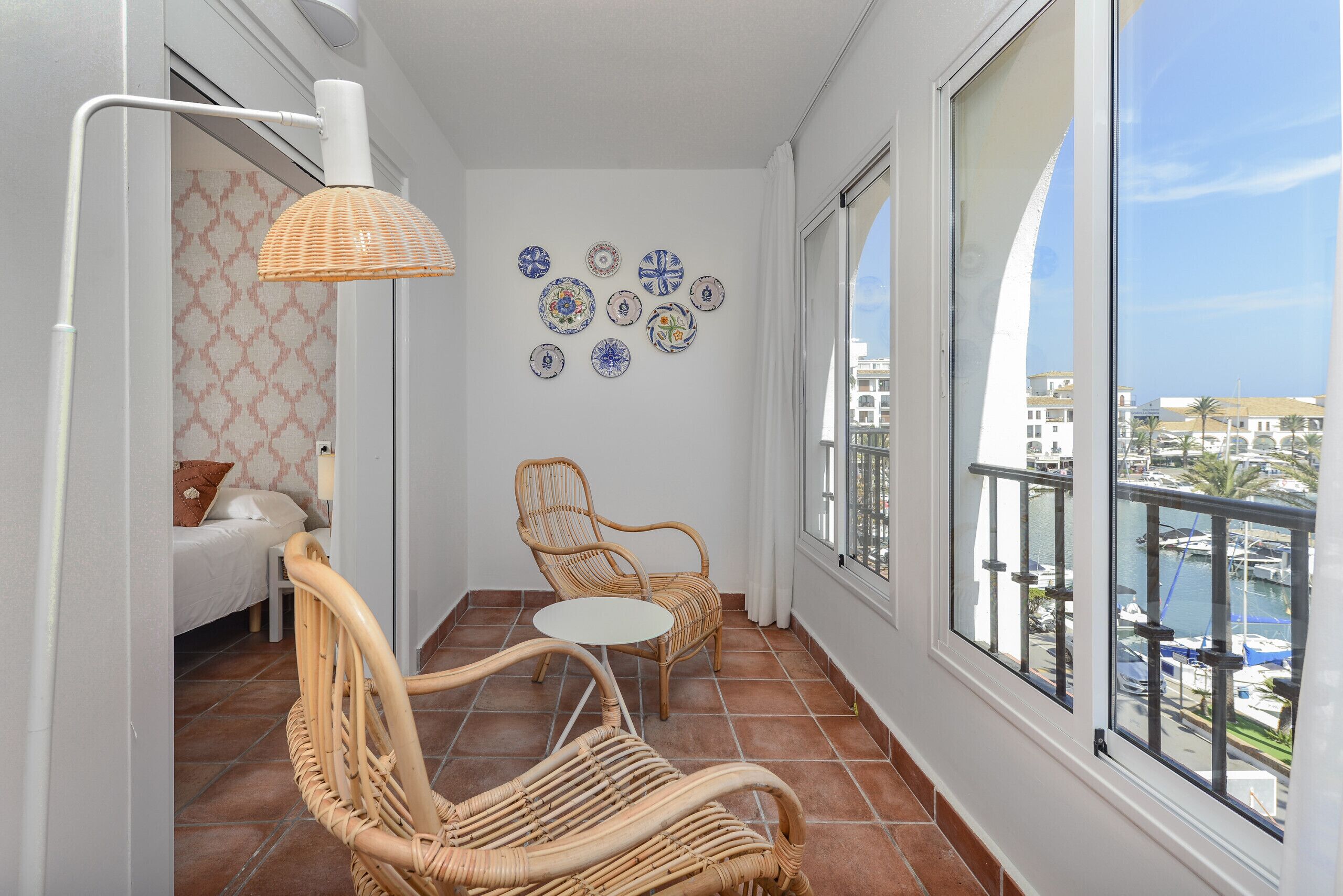 Ein Balkon mit Korbmöbeln, einem weißen Tisch und dekorativen Tellern an der Wand.