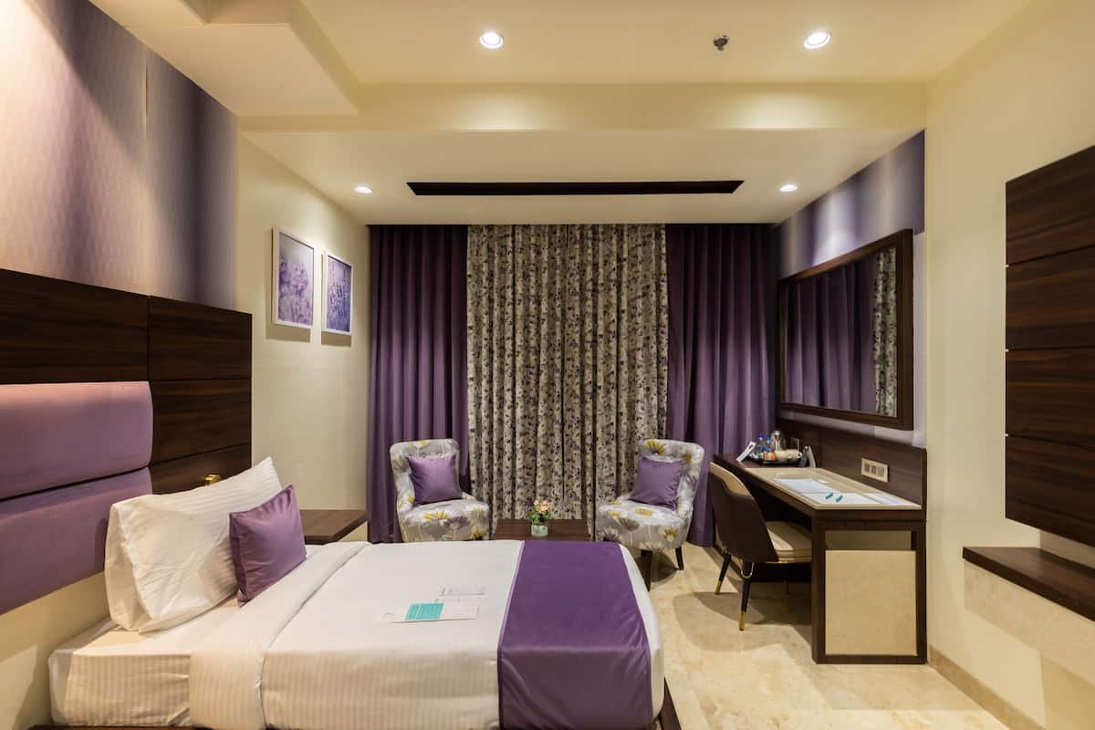 A hotel room with a bed, two chairs, a desk, and a large mirror.