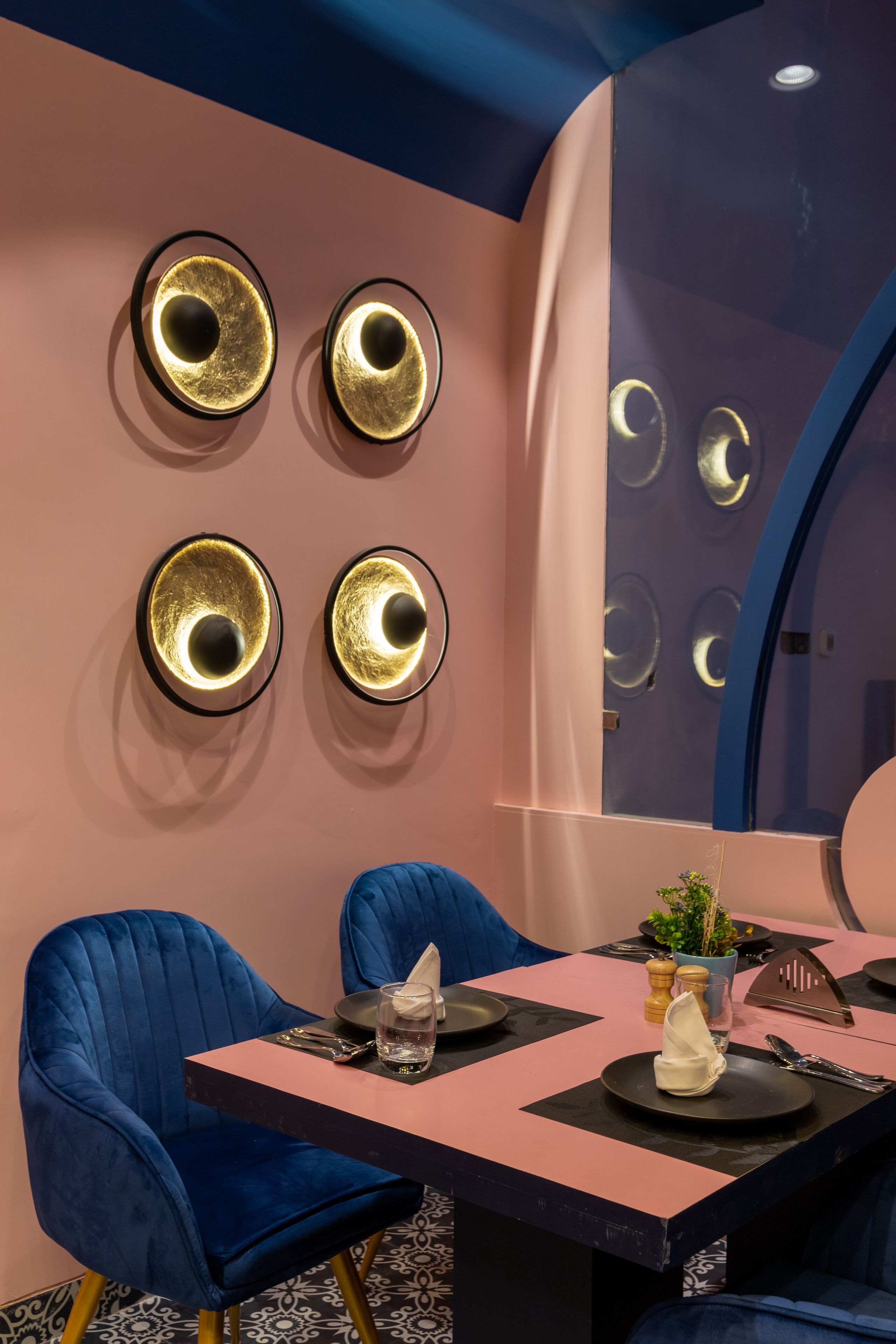 Un comedor moderno con una mesa rosa y negra, sillas tapizadas en azul y apliques decorativos en la pared.