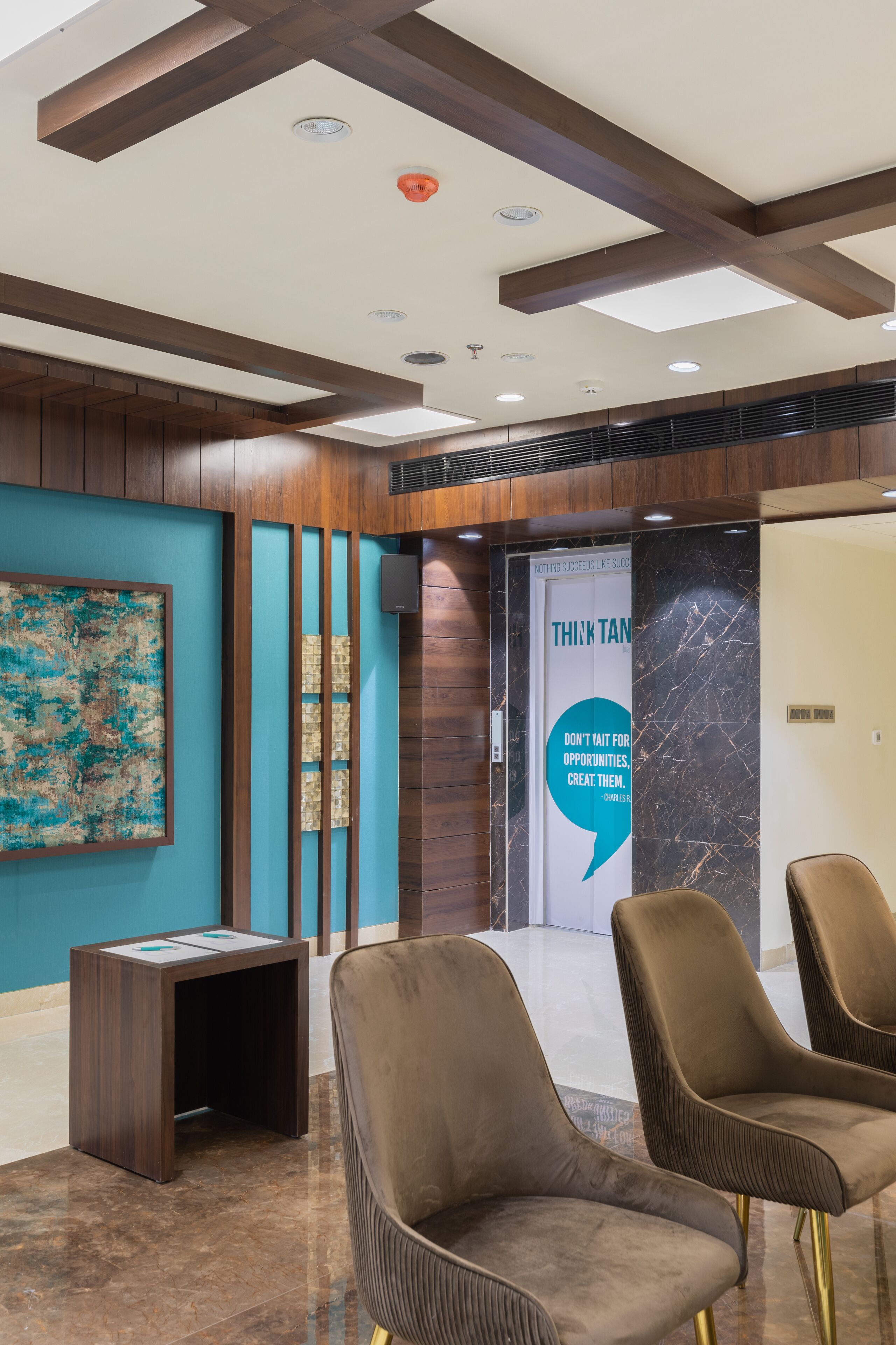 A lobby with wooden paneling, a blue wall with a textured artwork, a motivational quote on the wall, and two brown upholstered chairs.