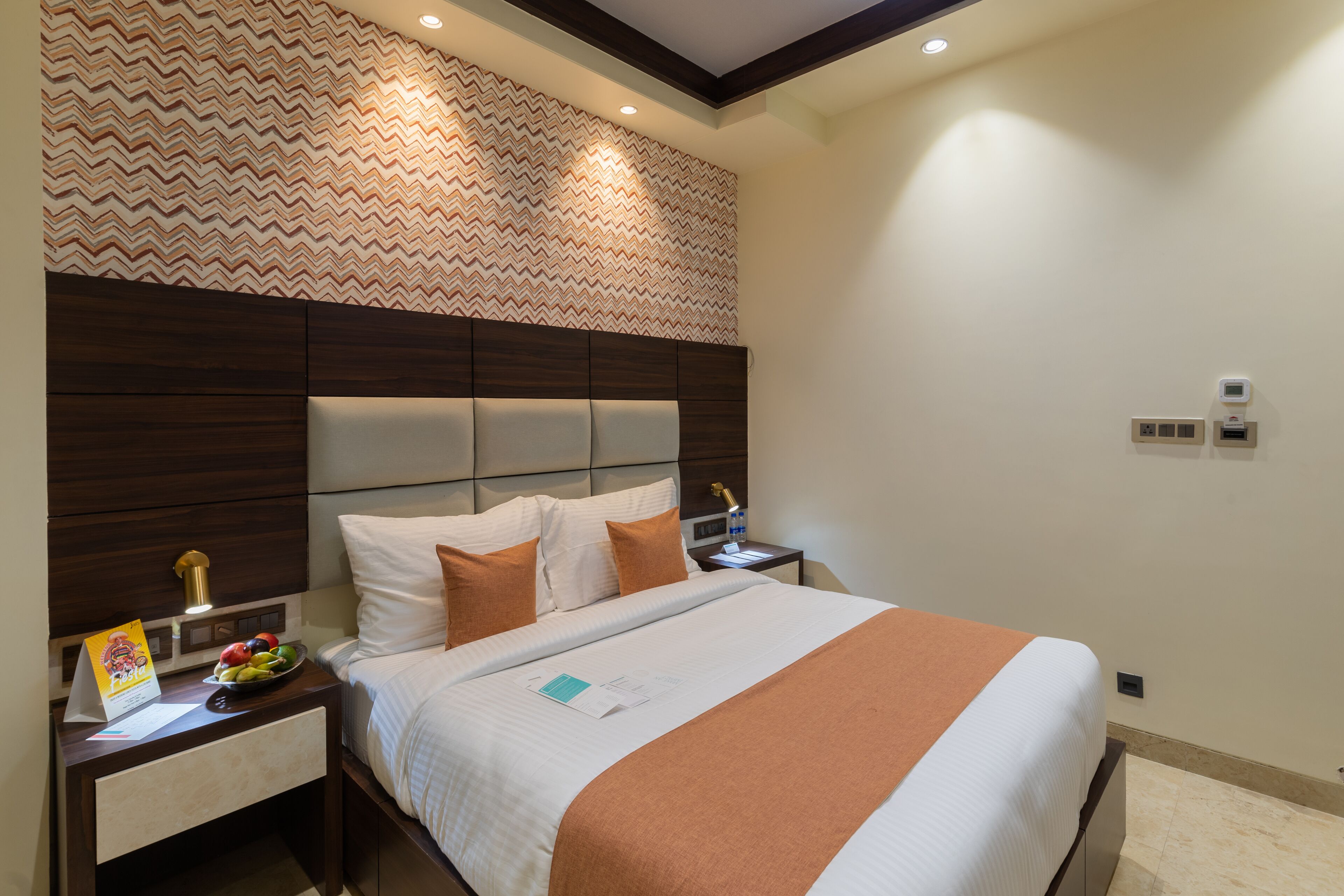 A hotel room with a bed, nightstands, a wall clock, and a patterned wallpaper.