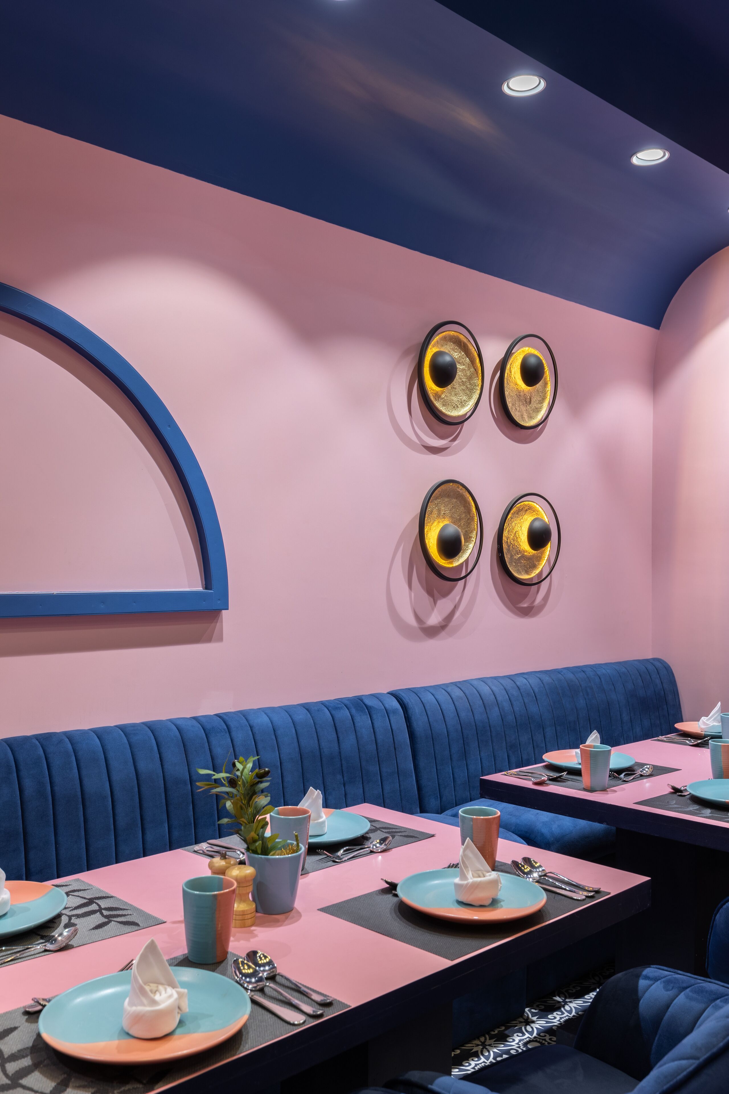 A restaurant with pink and blue color scheme, round tables, and blue cushioned booths.