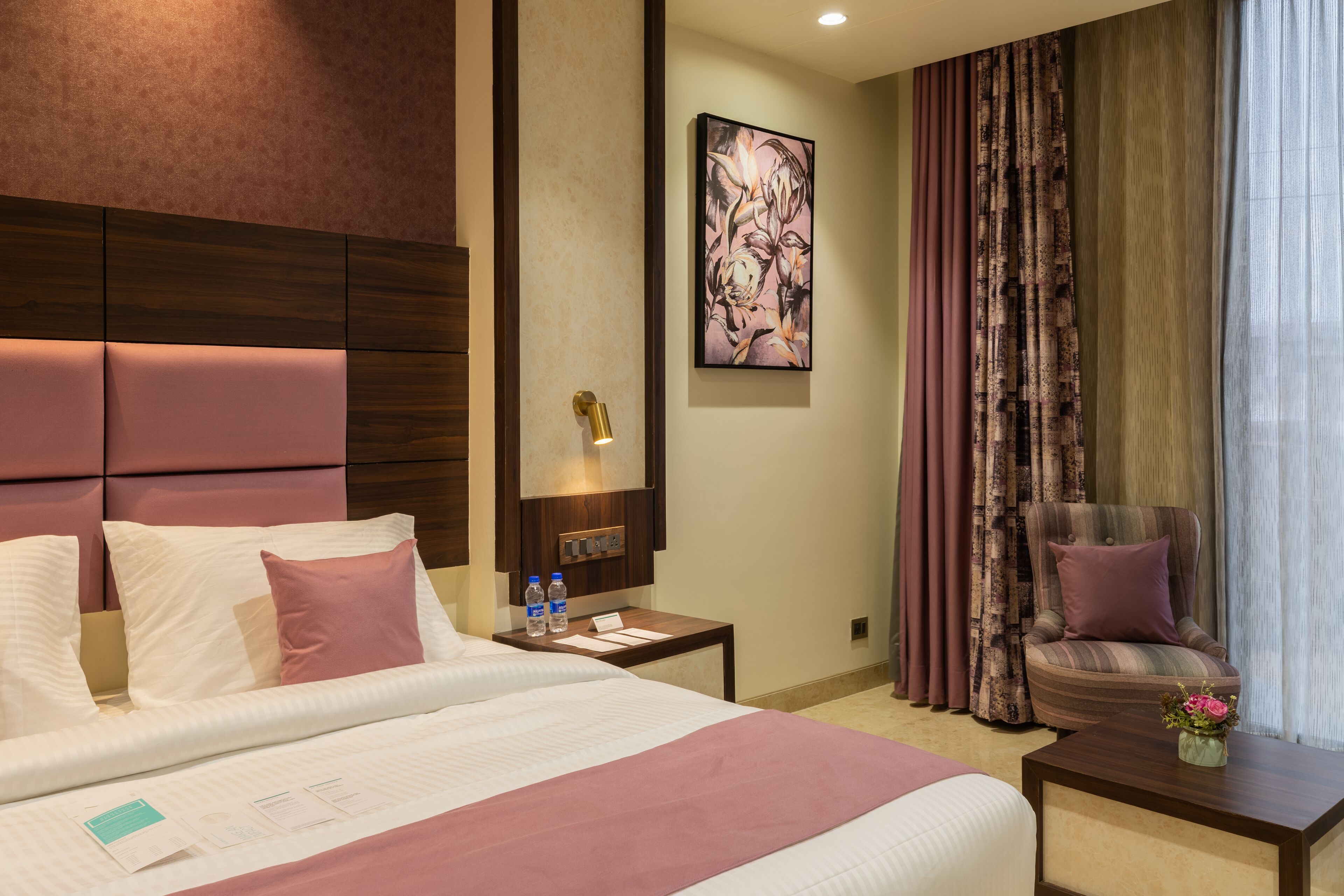 A hotel room with a large bed, a nightstand with a lamp, a chair, and a painting on the wall.