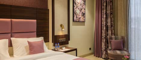 A hotel room with a large bed, a nightstand with a lamp, a chair, and a painting on the wall.