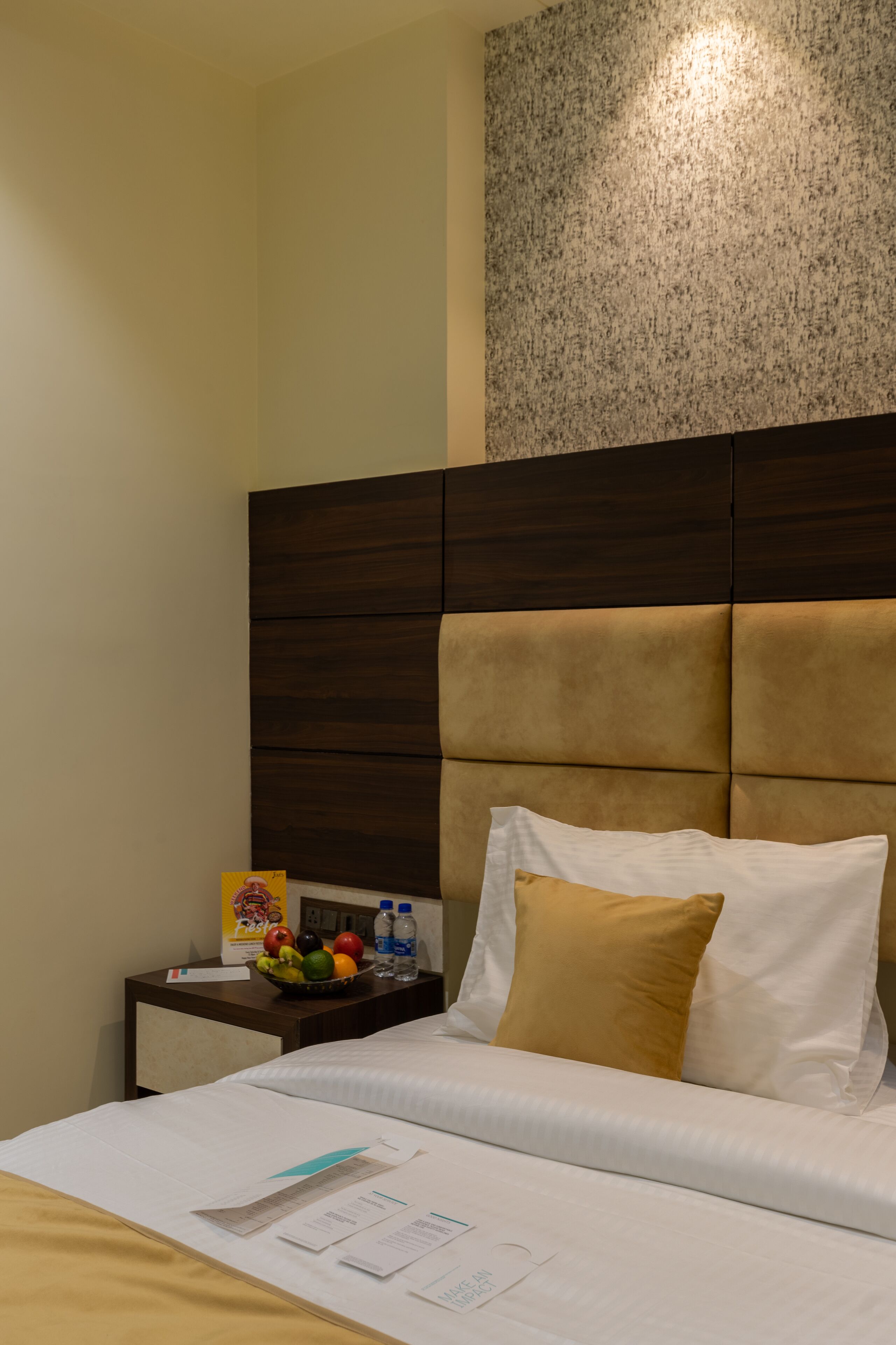 Habitación de hotel con cama, mesita de noche con frutero, botellas de agua y caja de pañuelos.