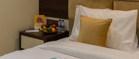 Habitación de hotel con cama, mesita de noche con frutero, botellas de agua y caja de pañuelos.