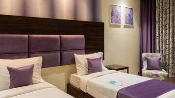 A hotel room with two beds, a wooden headboard, a floral armchair, and a nightstand with a lamp.