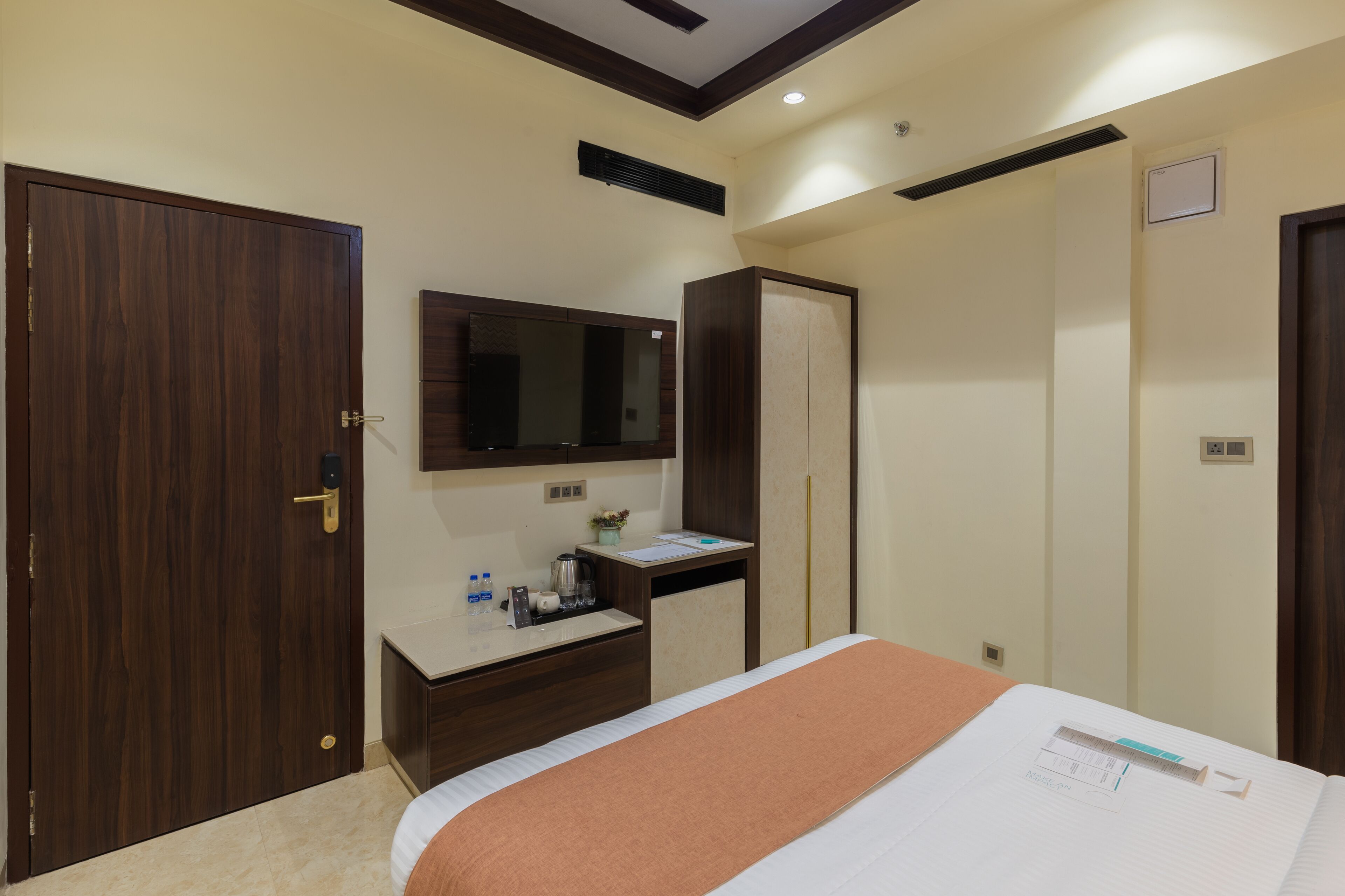 A hotel room with a bed, a desk with a mirror, a wardrobe, and a door.