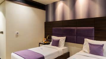 A hotel room with two beds, a wooden headboard, and a nightstand with a fruit bowl.