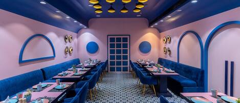 Un restaurante con decoración azul y rosa, varias mesas y un suelo estampado.