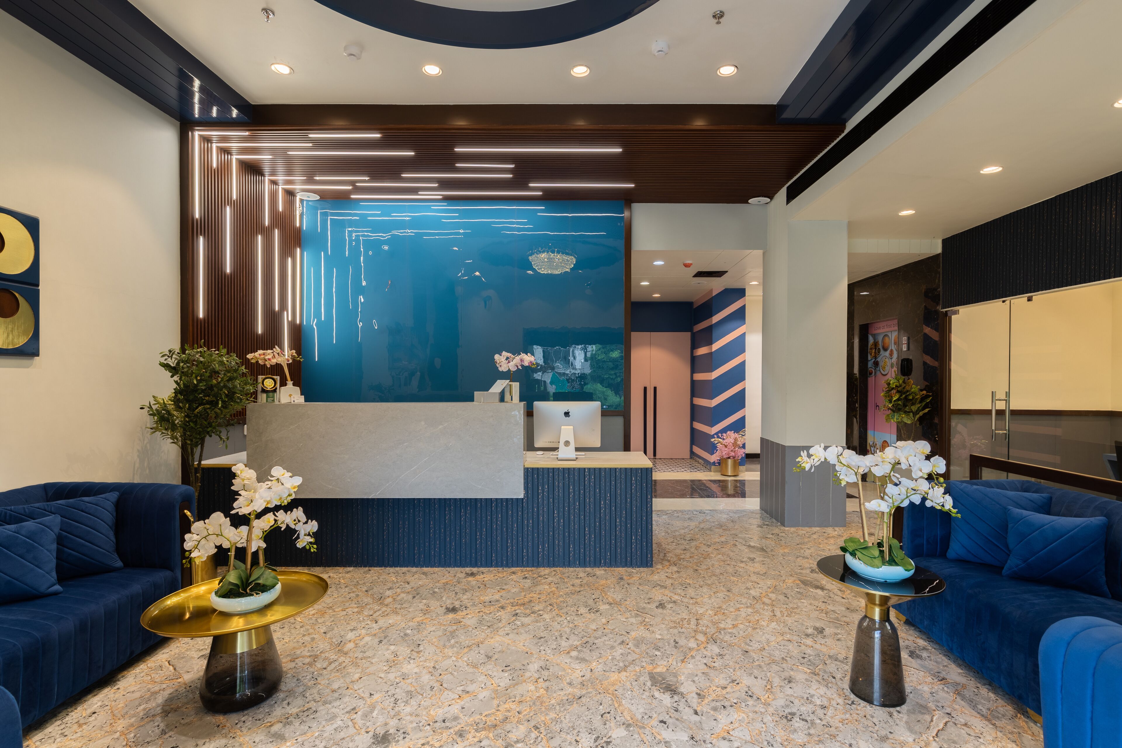 A modern reception area with a marble floor, blue sofas, and a reception desk with a computer.