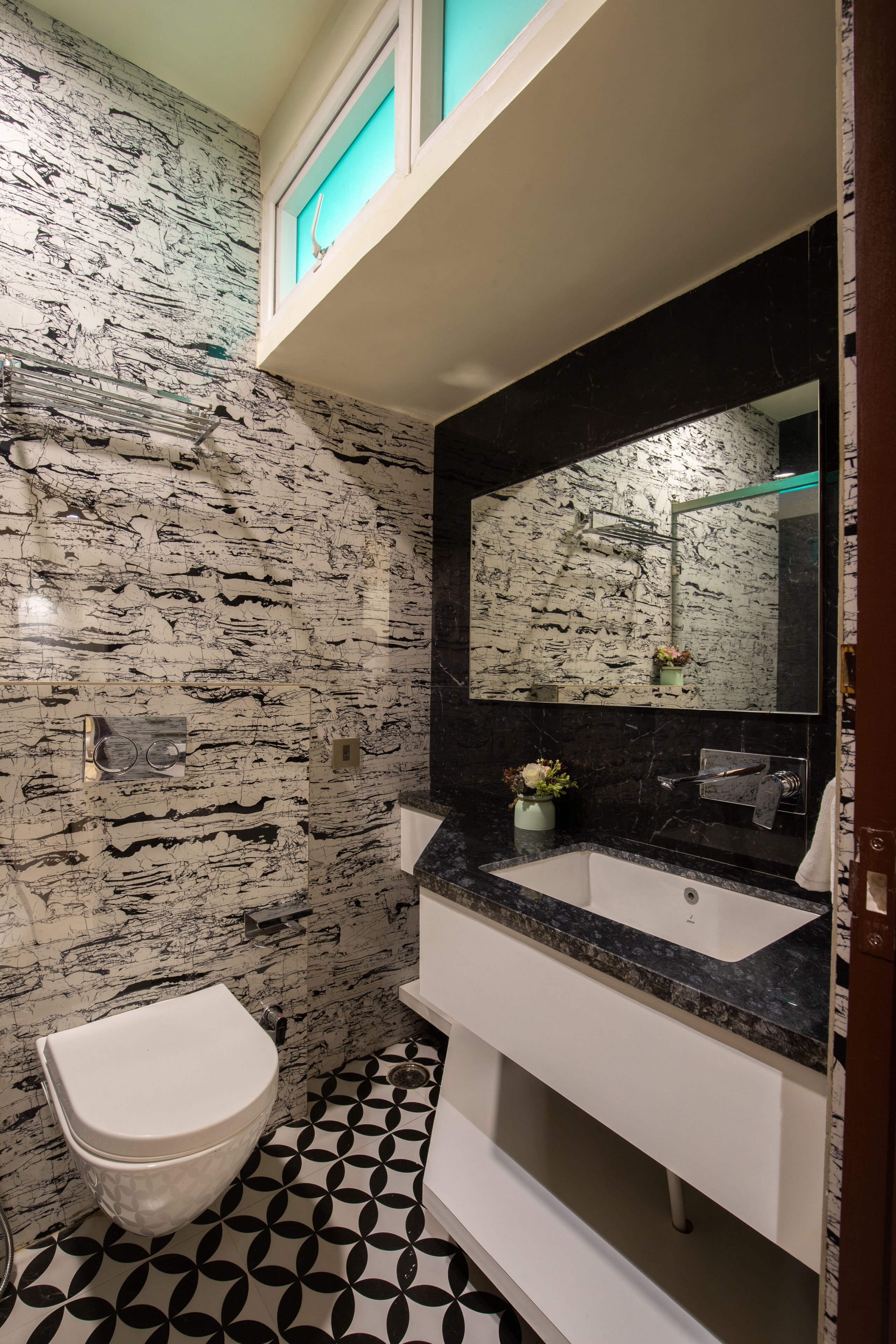 A bathroom with a marble wall, a white toilet, a sink with a black countertop, and a mirror above the sink.