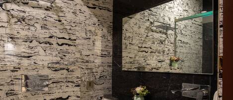 A bathroom with a marble wall, a white toilet, a sink with a black countertop, and a mirror above the sink.
