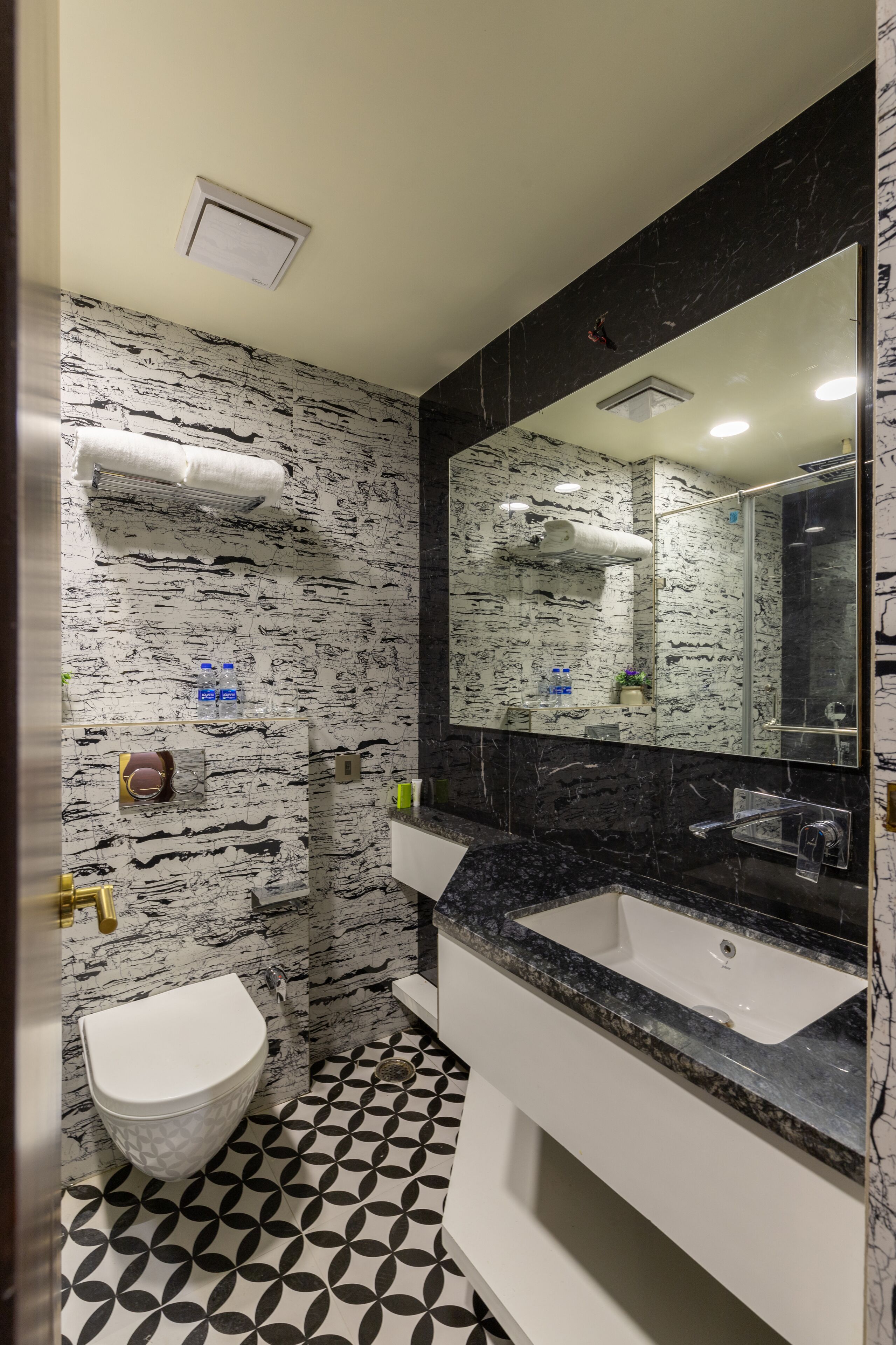 A bathroom with a white toilet, black and white patterned walls, a large mirror, and a black marble countertop.
