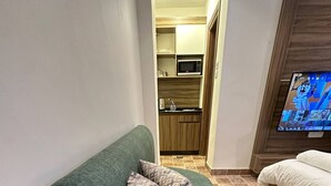A green sofa with patterned cushions, a television, and a kitchenette in the background. - 2, Antica Jabalal-lwebdeh (Amman)