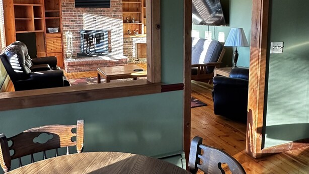 A dining area with a table, chairs, and a tray of strawberries. A brick fireplace and wooden shelves are visible in the background. - Cute Two Bedroom Cottage in Quiet Setting (Aberdeen)