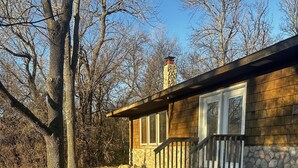 A single-story house with a stone foundation, a wooden deck, and a stone chimney. - Cute Two Bedroom Cottage in Quiet Setting (Aberdeen)