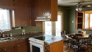 A kitchen with wooden cabinets, a stove, and a dining area with a table and chairs. - Cute Two Bedroom Cottage in Quiet Setting (Aberdeen)