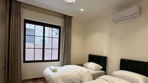 A hotel room with two beds, a large window, a ceiling light, and an air conditioning unit.