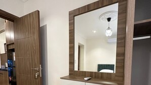 A hotel room with a wooden wardrobe, a vanity with a mirror, a bench, and patterned floor tiles.