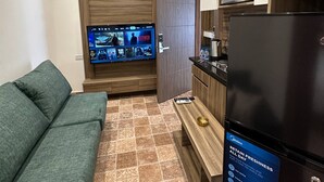 A compact living space with a sofa, a TV mounted on a wooden panel, a refrigerator, and a microwave.