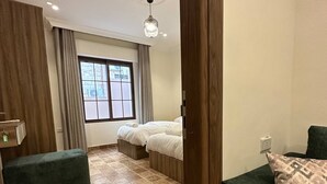 A hotel room with a bed, a green sofa, a patterned floor, a window with curtains, and a ceiling light.