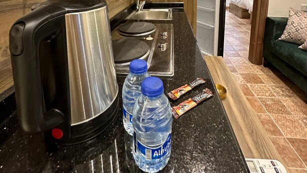 A kitchen with a kettle, water bottles, a scale, and a remote control on the counter.