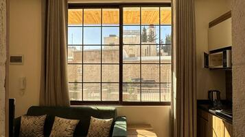 A room with a sofa, a window with curtains, a ceiling light fixture, and a kitchen area with a microwave.