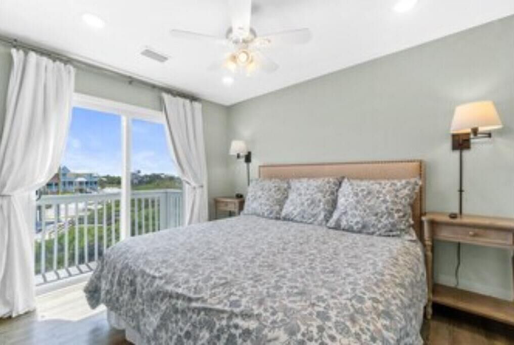 A bedroom with a large bed, a ceiling fan, and a view of the outdoors.