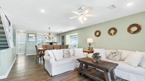 A spacious living room with a white sofa, a wooden coffee table, and a dining area in the background.