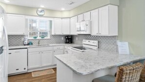 A modern kitchen with white cabinetry, a marble countertop, and a built-in microwave.