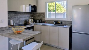 Una cucina moderna con forno a microonde, bollitore e tostapane sul piano di lavoro. Una finestra offre luce naturale e c'è un frigorifero a destra.