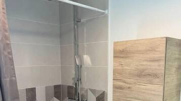 Une douche avec une porte en verre, un meuble en bois doté de tiroirs et un sol orné d’un motif de galets.
