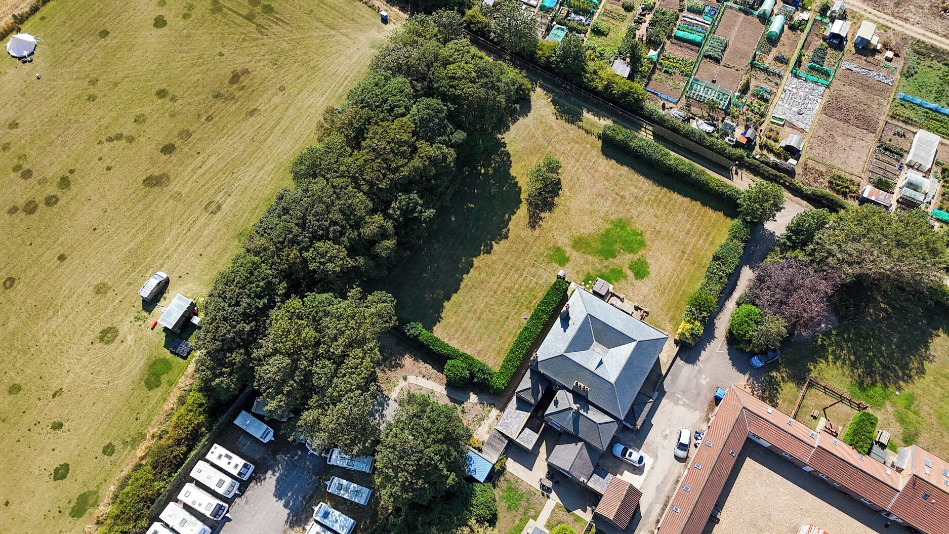 Vista aérea de una zona residencial con una casa grande, varias casas móviles y un campo.