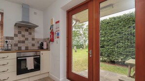 Een keuken met een inbouwoven, een magnetron en een broodrooster. Aan de muur hangt een brandblusser en er is een raam met uitzicht op een tuin.