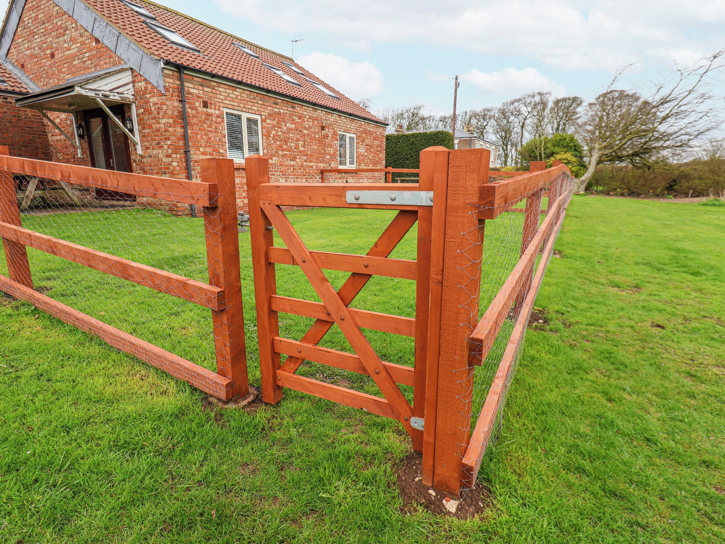 A wooden gate with a metal latch, a brick house with a tiled roof, and a grassy yard.