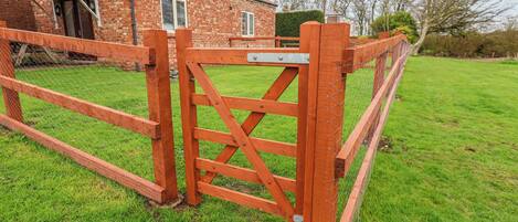 A wooden gate with a metal latch, a brick house with a tiled roof, and a grassy yard.