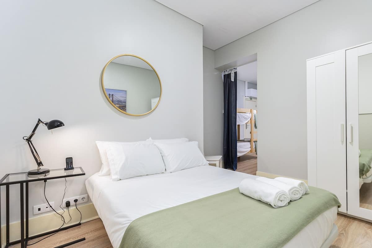 Een moderne hotelkamer met een opgemaakt bed, een nachtkastje met lamp, een ronde spiegel en een garderobe.