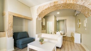 A modern living room with a stone archway, a grey sofa, a white coffee table, and a small table with a plant. - Metropolitan Lisbon Janelas Verdes (Lisbon)