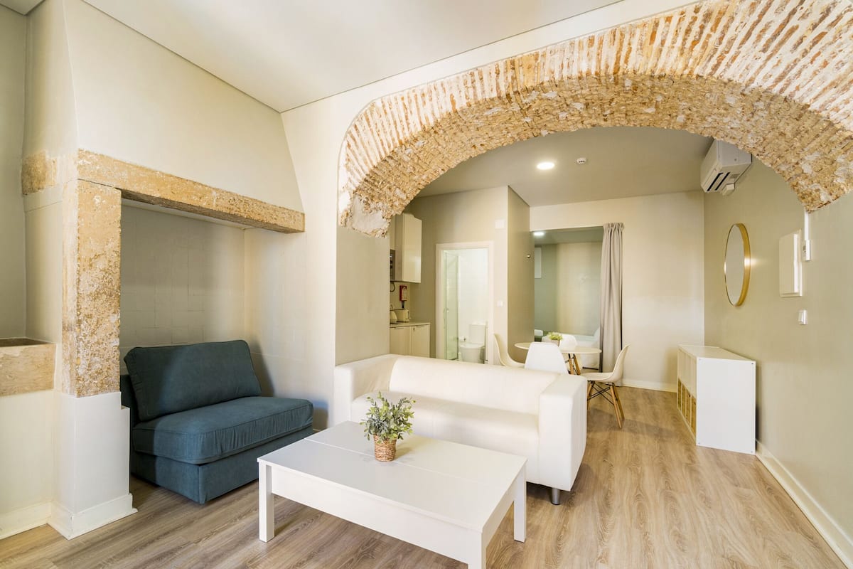Een moderne woonkamer met een stenen boog, een grijze bank, een witte salontafel en een bijzettafeltje met een plant.