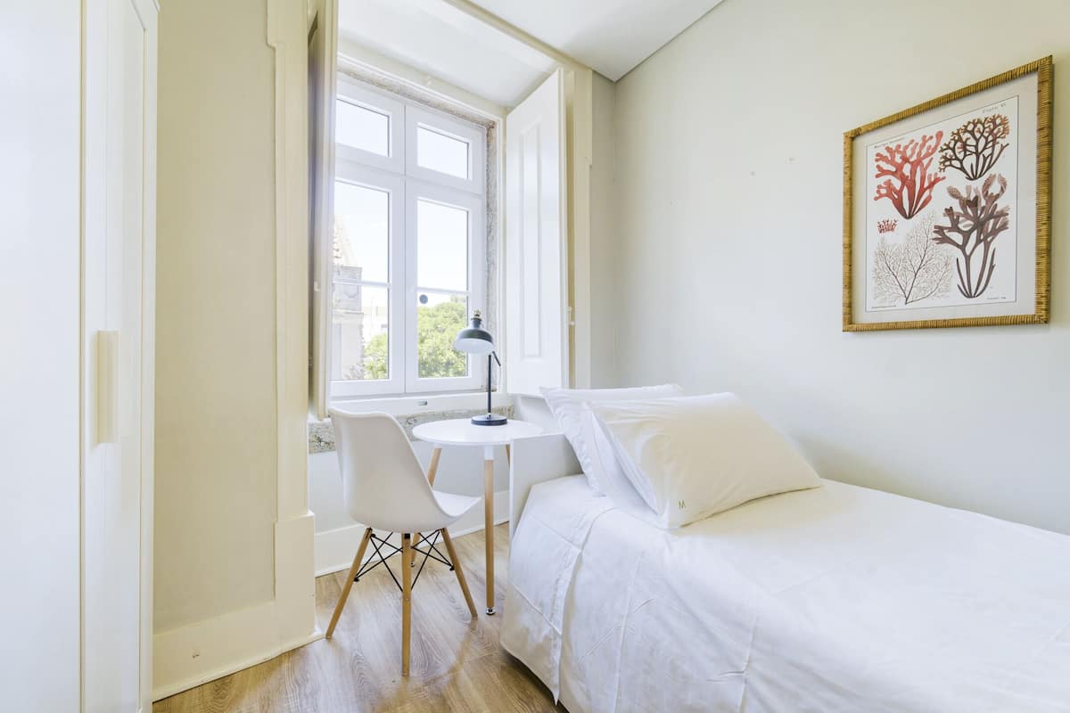 Een slaapkamer met een bed, een bureau en een stoel. Er is een raam met uitzicht op het omliggende landschap.