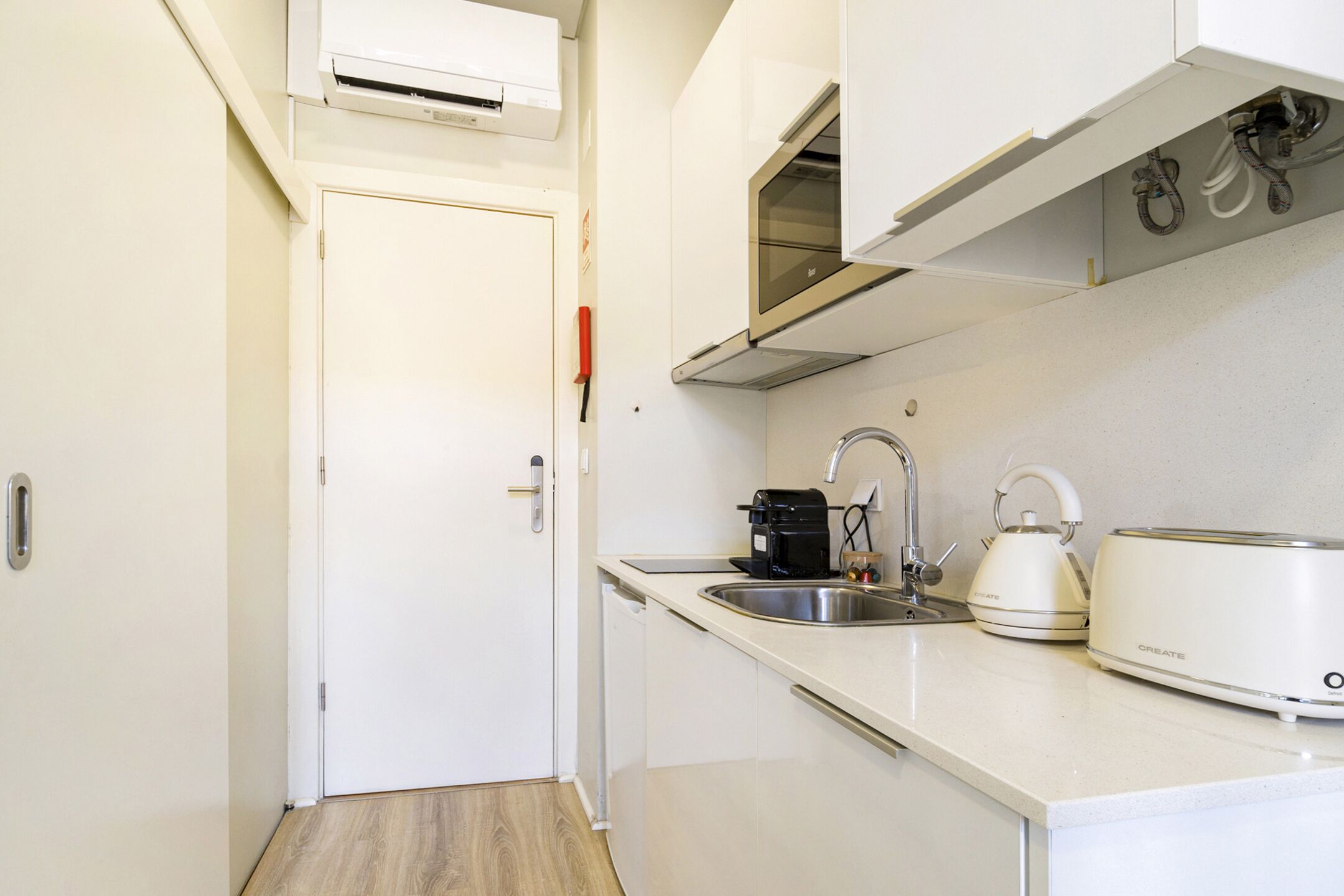 A compact kitchen with a white countertop, a coffee maker, a kettle, and a toaster.