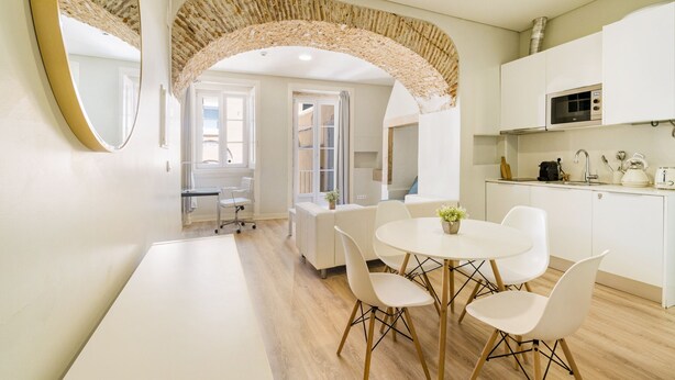 A modern kitchen with white cabinets, a microwave, and a stove. There is a dining area with a white table and chairs. - Metropolitan Lisbon Janelas Verdes (Lisbon)