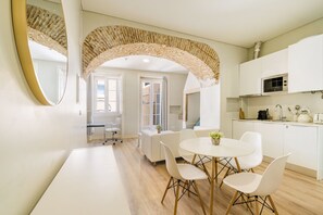 A modern kitchen with white cabinets, a microwave, and a stove. There is a dining area with a white table and chairs. - Metropolitan Lisbon Janelas Verdes (Lisbon)