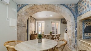 A dining area with a round table and wicker chairs, an arched stone doorway, and tiled walls. - Metropolitan Lisbon Janelas Verdes (Lisbon)