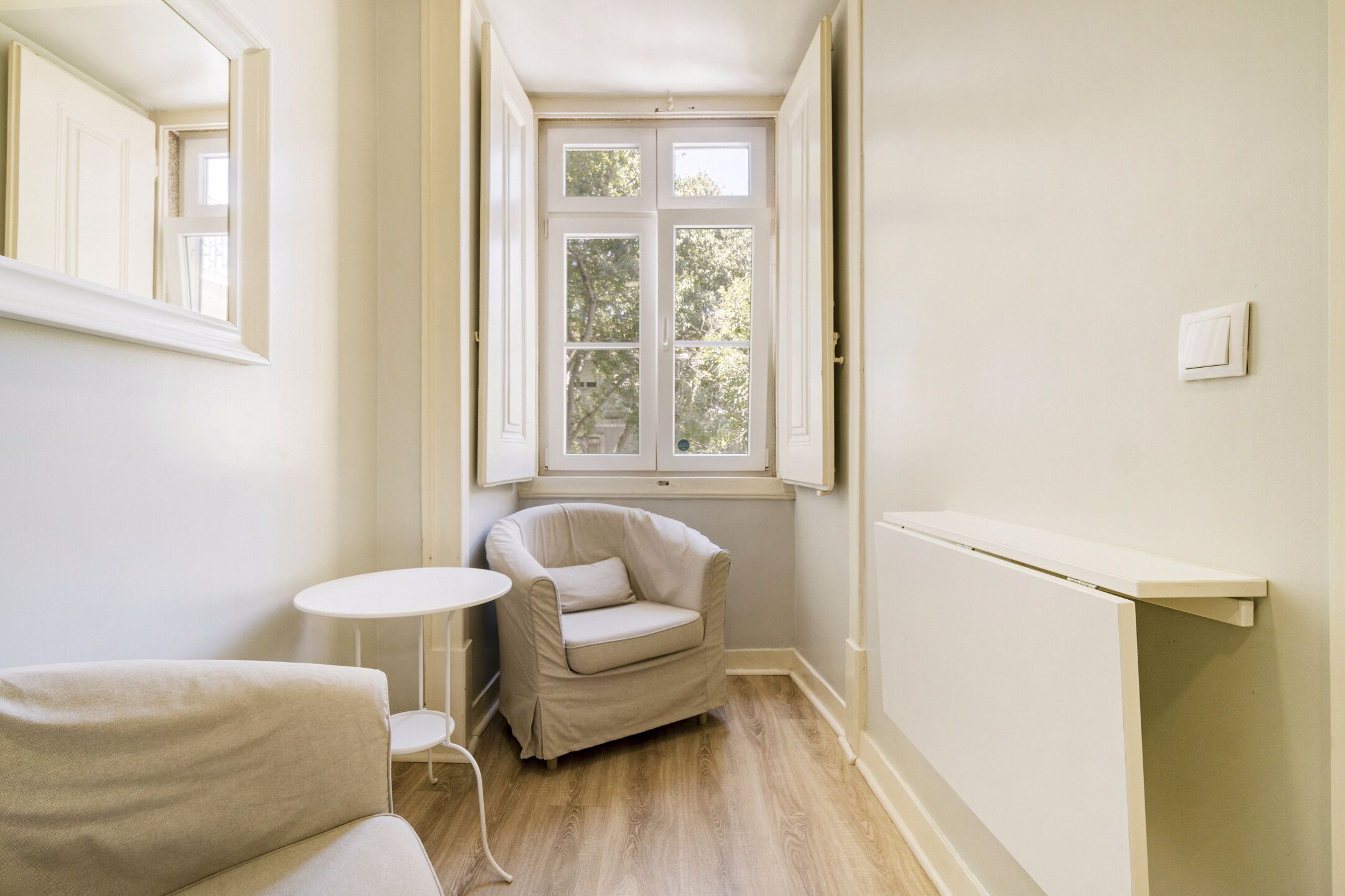 A room with a window, a chair, a small table, and a radiator.
